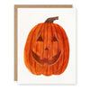 A white greeting card featuring a watercolor-style orange jack-o'-lantern pumpkin with a carved smiling face, shown with a brown kraft envelope behind it on a white background.