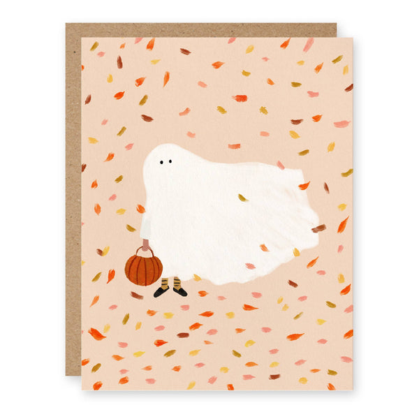 A greeting card with a whimsical illustration of a Halloween costume ghost with pumpkin trick-or-treat buket with an autumnal confetti backdrop, paired with a kraft paper envelope.