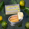 An opened tin of tuna belly in olive oil with the packaging next to it against a glossy green background with yuzu fruits. 