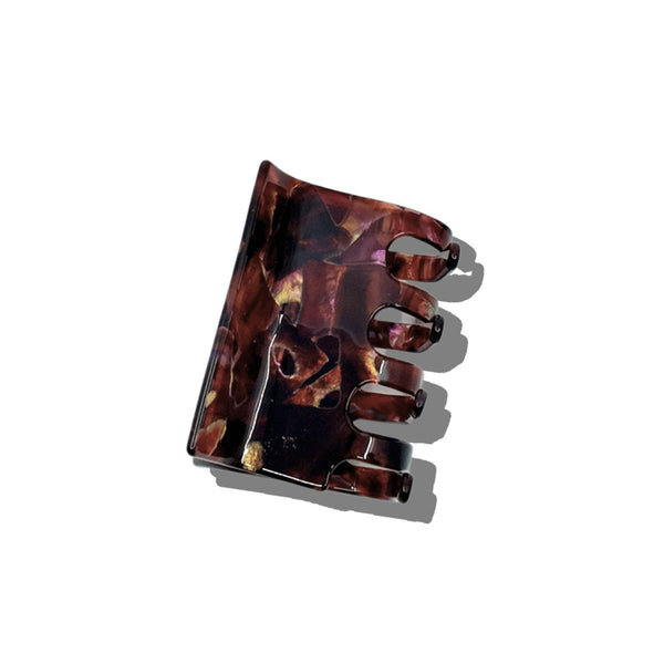A rectangular claw clip in a tortoiseshell color with iridescent purple and gold accents photographed on a white backdrop.