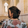 Person wearing a floral blouse with their hair half held up by a dark hair claw in an indoor setting