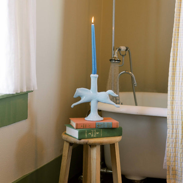 Blue candle on a decorative light blue horse shaped candle holder with books in a bathroom setting.