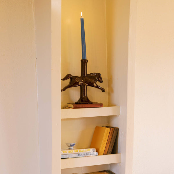 Small shelf with books and a horse shaped candle holder holding a dark blue taper candle.