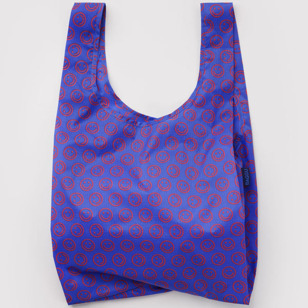 A nylon shopping bag in vibrant cobalt blue with mini red smiley faces on a white backdrop.