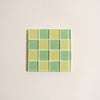 Square mosaic tile coaster with green and yellow checkered pattern on a beige background