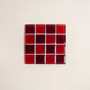 A glass mosaic tile coaster in red and dark red colors against a neutral background.