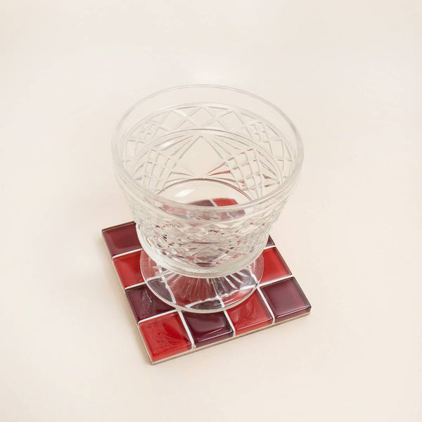 Clear glass on a red and dark red mosaic coaster with a neutral background