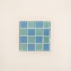 Square mosaic tile coaster with a grid of blue and green squares on a beige background