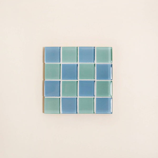 Square mosaic tile coaster with a grid of blue and green squares on a beige background