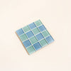 Square tile coaster with blue and green mosaic pattern on a beige background