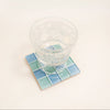 Clear glass on a square, blue and green checkered coaster with a white background