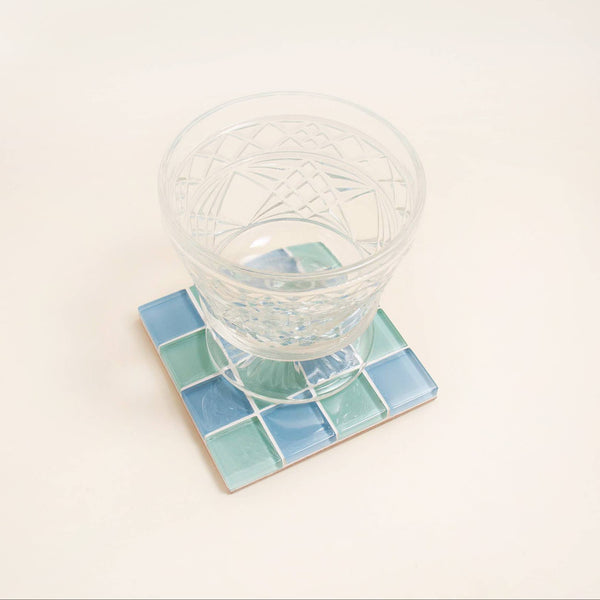 Clear glass on a square, blue and green checkered coaster with a white background