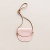 A kid's pale pink leather crossbody bag with brown leather strap against a neutral backdrop.
