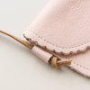 Close-up of a pale pink leather purse and the natural leather adjustable strap on a neutral backdrop.