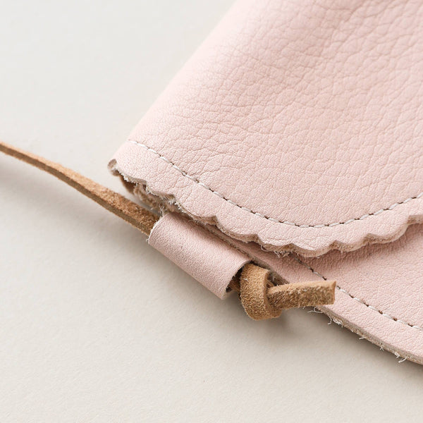 Close-up of a pale pink leather purse and the natural leather adjustable strap on a neutral backdrop.