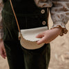 Child holding a small white handbag with a brown strap against a blurred background