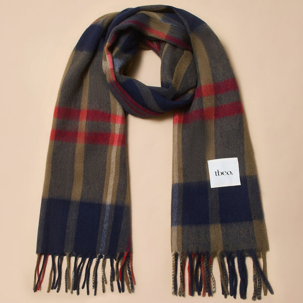 A large fringed lambswool scarf in a rich navy, olive green, red, and white tartan plaid against a neutral background.