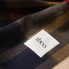 A detailed view of a white fabric 'tbco' brand tag on a richly colored plaid scarf.