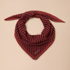 A fine knit triangle scarf in berry red and chestnut stripes twisted against a neutral background.