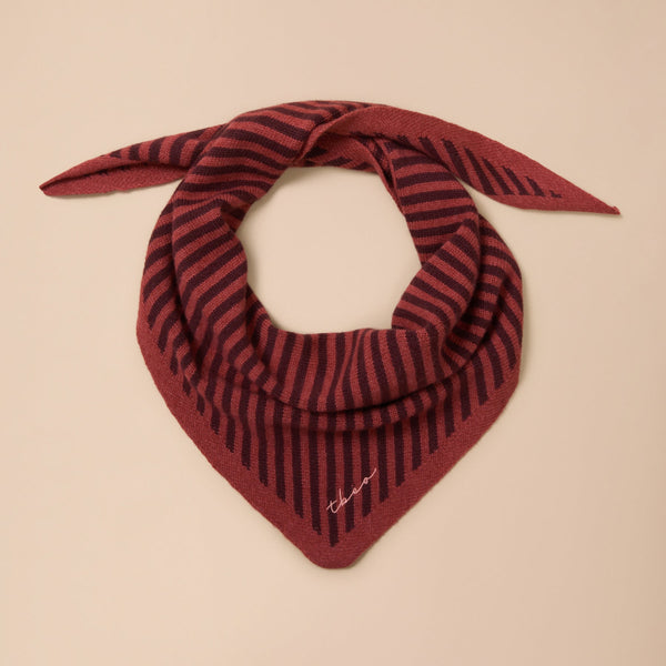 A fine knit triangle scarf in berry red and chestnut stripes twisted against a neutral background.