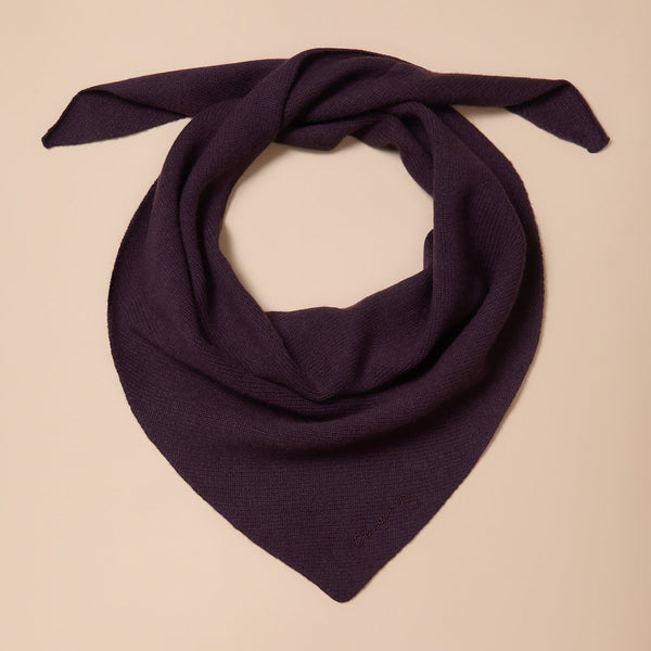A dark purple fine knit triangle shaped scarf twisted against a neutral background. 
