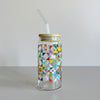 A glass travel cup with bamboo lid and glass straw. The cup is printed with a colorful quilt design featuring chickens, hearts, and suns.