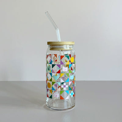 A glass travel cup with bamboo lid and glass straw. The cup is printed with a colorful quilt design featuring chickens, hearts, and suns.