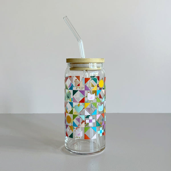 A glass travel cup with bamboo lid and glass straw. The cup is printed with a colorful quilt design featuring chickens, hearts, and suns.