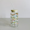 A glass travel cup with bamboo lid and glass straw. The cup is printed with a colorful fish design.