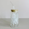 A glass travel cup with bamboo lid and glass straw. The cup is printed in a whimsical white floral design.