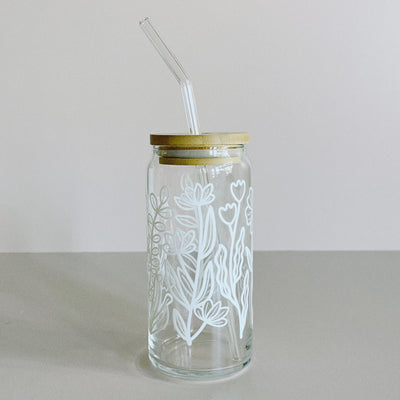 A glass travel cup with bamboo lid and glass straw. The cup is printed in a whimsical white floral design.