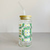 A glass travel mug featuring a white, yellow, and green daisy quilt print. The cup includes a bamboo lid and glass straw. 