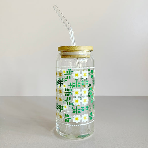 A glass travel mug featuring a white, yellow, and green daisy quilt print. The cup includes a bamboo lid and glass straw. 