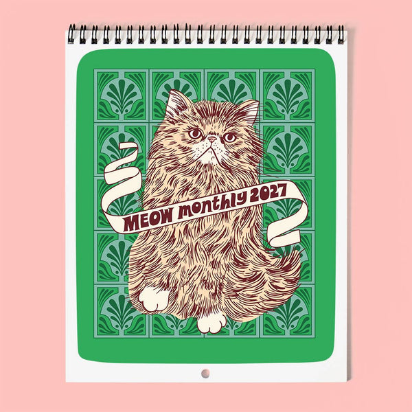Wire-bound wall calendar with a cat illustration and 'Meow Monthly 2027' text on a green tile patterned background, against a soft pink surface.