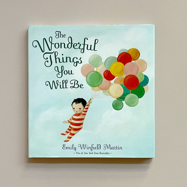 A children's book called 'The Wonderful Things You Will Be' featuring an illustration of a young child floating while carrying a bunch of colorful balloons. The book sits against a neutral backdrop.
