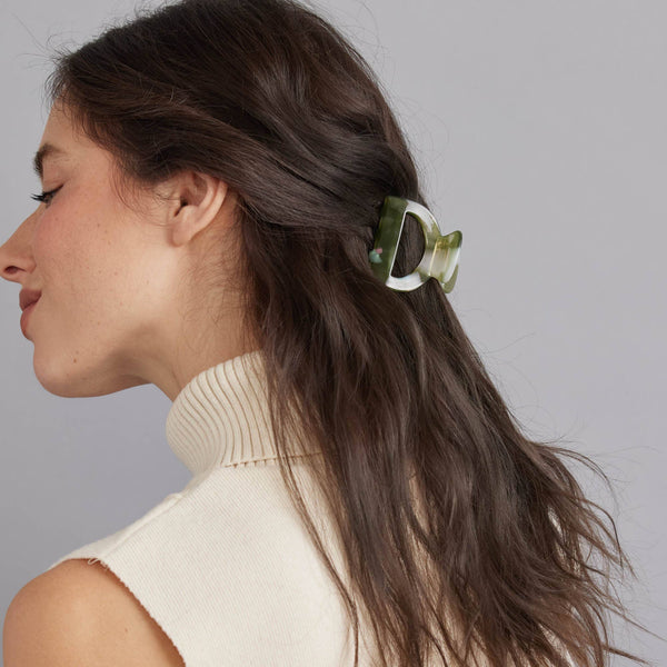 A person with a half ponytail held back by a small arch hair claw against a grey background.