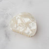 Small pearly iridescent white oblong hair claw on a white marble background.
