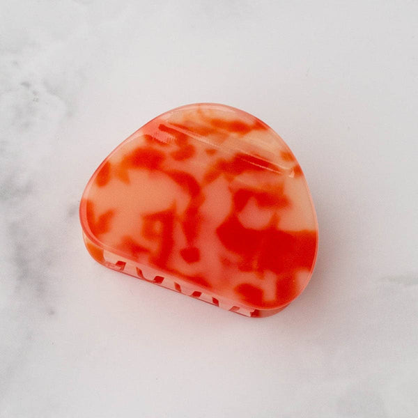 Orange and white marbled oblong hair claw on a light gray marble background