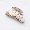 A cream, tan, and brown speckled hair claw on a white marble background.