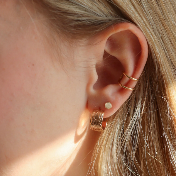 Close-up of an ear wearing gold hoop earrings with a soft focus on hair and skin.