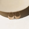 A pair of minimalist crescent moon-shaped drop earrings in a matte gold finish, displayed on a light beige ceramic plate against a white background.