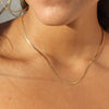 Gold necklace on a person's neck with a neutral background