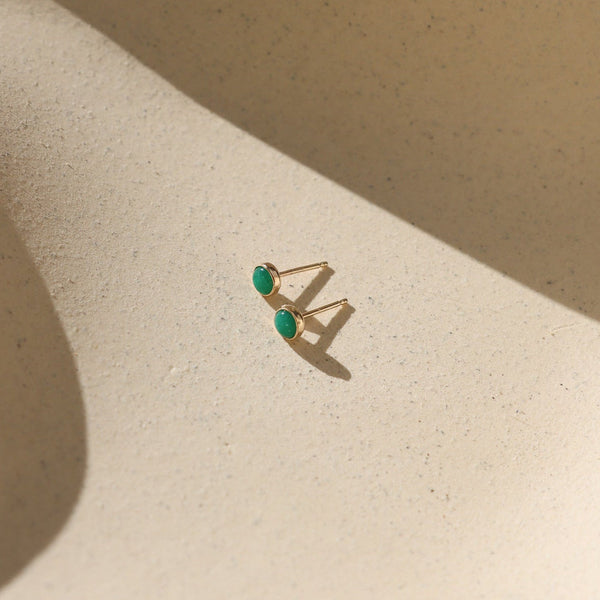 Gold earrings with emerald gemstones on a beige surface