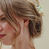Close-up of a person wearing gold earrings with turquoise beads against a neutral background