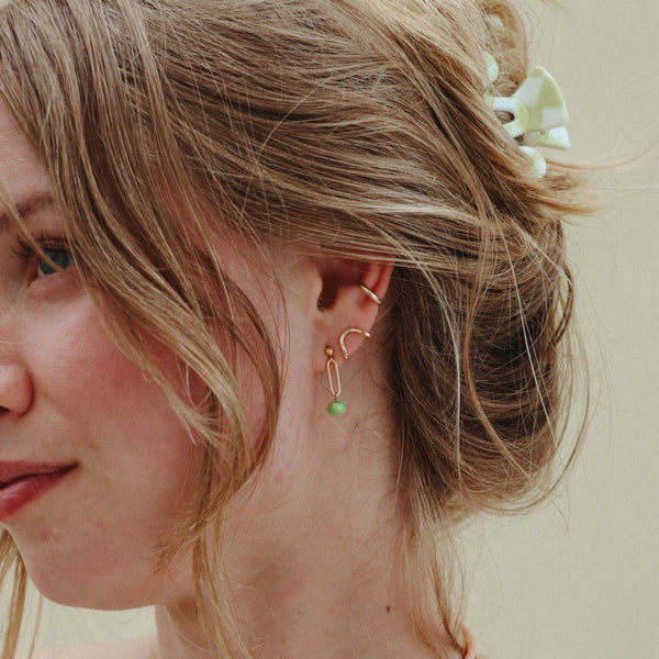Close-up of a person wearing gold earrings with turquoise beads against a neutral background