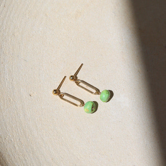 Gold earrings with turquoise beads on a beige background