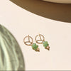 Gold earrings with green beads on a beige surface