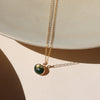 A fine gold chain necklace with an oval moss agate pendant against a shadowy neutral backdrop. 