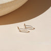 A pair of sterling silver hollow oval shaped stud earrings on a shadowy neutral background.