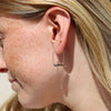 A person with blonde hair and freckles wearing a gold arch earring with jasper beads.